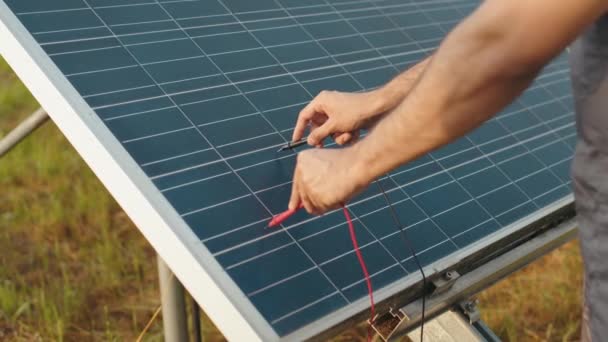 Erkek ellerinin kapalı olması güneş panellerindeki voltajı çoklu metre açık havada kontrol ediyor. Enerji teknisyeninin güneş istasyonunu kontrol etmesini sağlayın. Güneş panellerindeki voltajı çoklu metre ile kontrol eden adam — Stok video