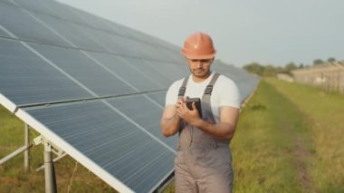 Üniformalı Hintli işçi, güvenlik kaskı ve güneş panellerini incelerken çoklu metre kullanan gözlükler. İnsanlar, bakım ve yeşil enerji kavramı. Güneş panellerindeki direnci kontrol eden mühendis