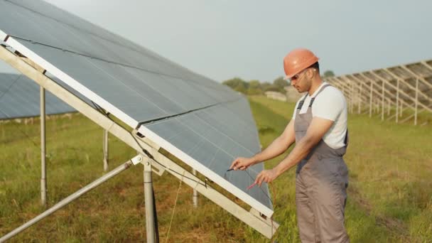 Técnico profesional de energía midiendo voltaje en células solares en estación al aire libre. Hombre indio en uniforme y casco realizando trabajo de servicio con multímetro. Tensión de medición en células solares — Vídeos de Stock