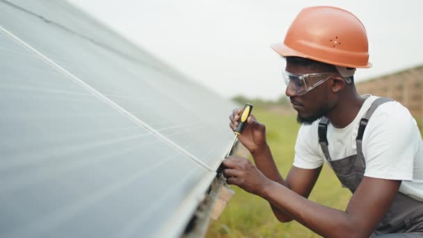 Técnico en casco y mono fijación de paneles solares con destornillador al aire libre. Trabajador que controla y mantiene el trabajo de la estación solar. Hombre en uniforme usando destornillador para reparar paneles solares — Vídeos de Stock