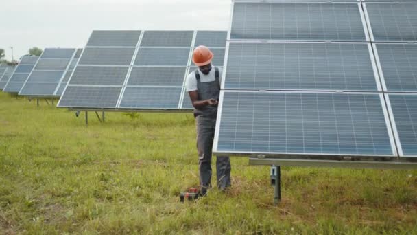 Maintenance et énergies alternatives. Technicien professionnel en uniforme utilisant le multimètre tout en vérifiant la tension dans les panneaux solaires. Contrôle afro-américain de la production d'énergie verte sur la station. — Video