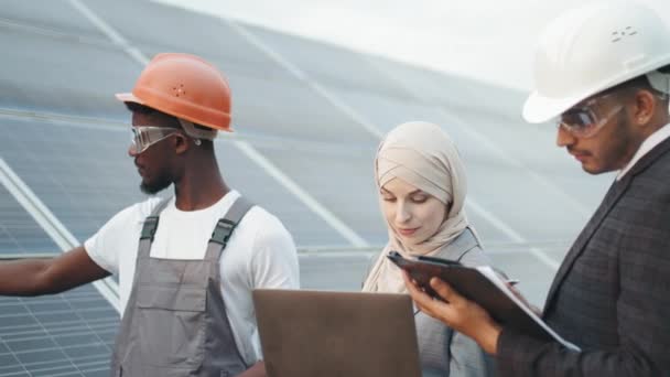 Industrial worker showing thermal imager with indexes to inspectors. Inspection on solar station. Muslim woman and indian man standing with african technician and checking temperature of solar panels. — Stock Video
