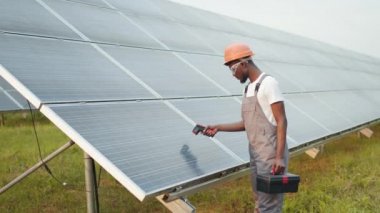 Erkek elinin açık havada güneş pilinin yanında elektronik termal görüntüleyiciyi tutarken yakın plan. İstasyondaki fotovoltaik panellerin sıcaklığını kontrol eden Afrikalı Amerikalı teknisyen.