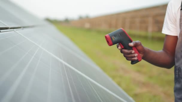 Närbild av manlig handhållen elektronisk värmekamera nära solceller utomhus. Afrikansk tekniker kontrollerar temperaturen på solcellspaneler på stationen. Kontroll av solpanelers värme — Stockvideo