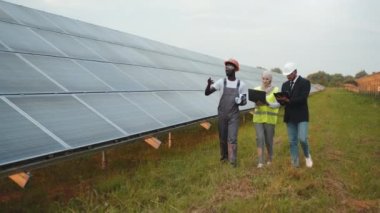Hintli işadamı ve Müslüman kadın güneş istasyonu içinde Afrikalı teknisyenle yürüyorlar. İki müfettiş dosya ve dizüstü bilgisayar kullanıyor. Alternatif enerji kavramı. Güneş çiftliğinde teftiş yapan insanlar