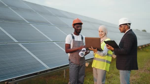 Comprobación de equipos granja solar. Técnico teniendo reunión con dos inspectores multirraciales en la estación solar. Hombre de negocios indio en casco blanco y mujer musulmana en equipo de verificación de hijab de la granja. — Vídeo de stock