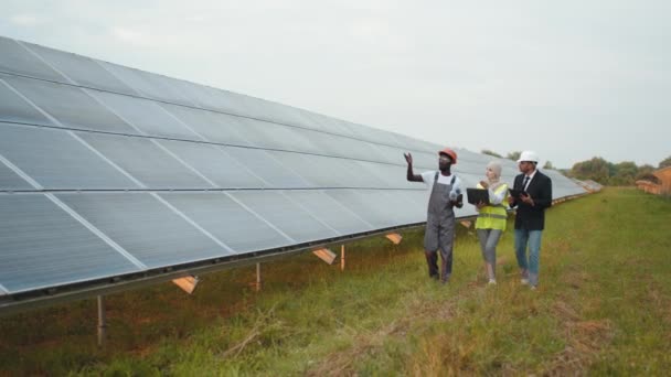 Persone multiculturali che fanno ispezioni in una fattoria solare. Tecnico che presenta la moderna stazione solare all'uomo indiano e alla donna musulmana. Due manager con laptop controllano la produzione di energia verde. — Video Stock