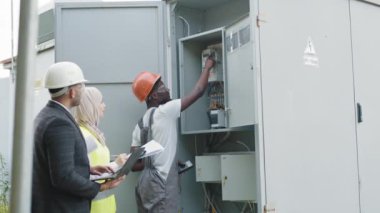 Güvenlik kasklı elektrikçi, elektrik devrelerindeki voltaj seviyelerini kontrol ediyor. Ekipman Güç Dağıtım Kabinesi. Elektrik Mühendisi Testi Voltaj Akım Elektrik Hattını Ölçüyor.