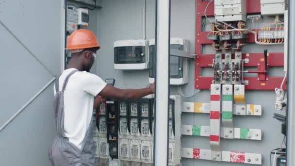 Mann in Uniform repariert Kabel in Schaltanlage im Solarpark Afrikanischer Mann repariert Kabel in Schaltanlagen an einer Solarstation. Konzept von Mensch, Wartung und alternativer Energie. — Stockvideo