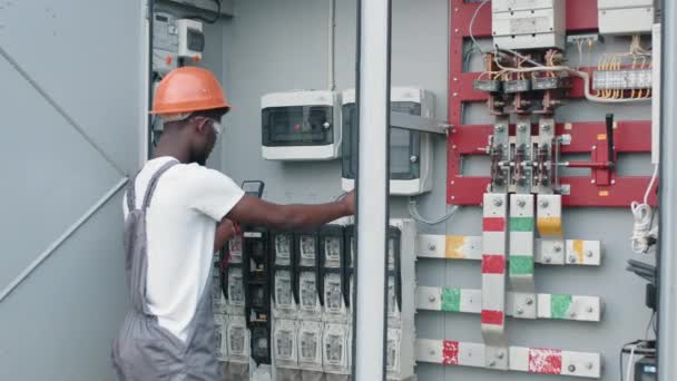 Hombre en uniforme reparando cables en aparamenta en granja solar. Hombre afroamericano reparando cables en aparamenta en la estación solar. Concepto de personas, mantenimiento y energía alternativa. — Vídeo de stock