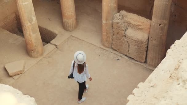 Вид зверху на молоду кавказьку жінку в білому літньому капелюсі та одязі, що ходить на руїнах стародавнього храму та вивчає збережені колонки. Археологія та концепція людей. Археологічне копання — стокове відео