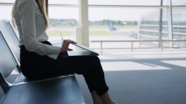 Havaalanında dizüstü bilgisayarda oturan genç ve güzel bir kadın. Kız turist serbest çalışıyor ve bekleme odasında uçmayı bekliyor. Konsept seyahat, uzaktan çalışma. Laptop kullanan bir bayanla havaalanı salonu.
