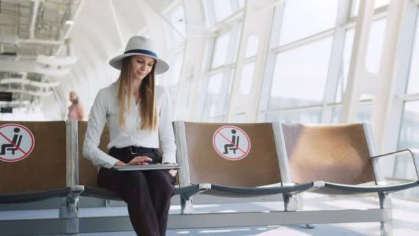 Departure lounge with a woman typing on a laptop. Girl tourist freelancer works and waits for flight in waiting room. Concept travel, remote work. Silhouette against the background of a large window. — Stock Video