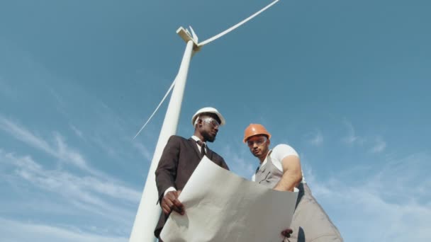 Inspetor e engenheiro estão inspecionando um projeto em um campo de turbinas eólicas que produz eletricidade. Conceito de energia limpa energia renovável, salvar o mundo. Colegas falando em campo com turbinas eólicas — Vídeo de Stock