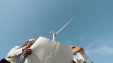 Rüzgâr türbininin planlarını incelerken, güvenlik miğferlerinde dört çok ırklı ortak. Yetenekli endüstriyel işçiler ortak projeyi tartışıyor. Temiz enerji kavramı, yenilenebilir enerji, dünyayı kurtarmak..