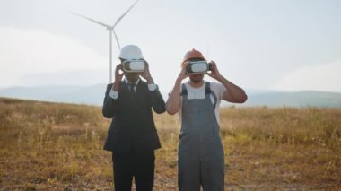 Amerikalı işadamı ve Hintli mühendis rüzgâr türbinleriyle çiftlikte yaptıkları toplantıda VR kulaklık takıyorlar. Yenilikçi teknolojiler ve alternatif enerji kavramı. Eko çiftliğindeki toplantı sırasında VR kulaklığı