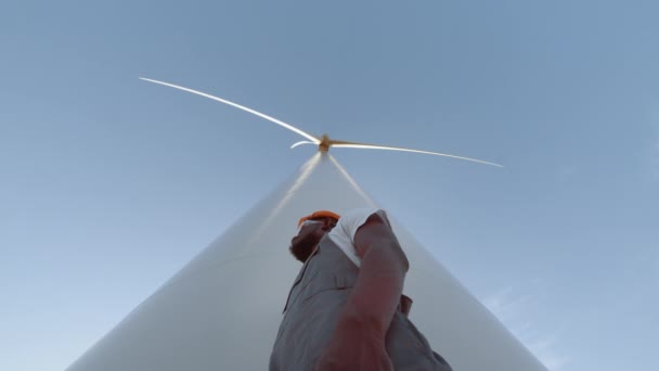 Engenheiro sorridente perto de turbinas eólicas, desenvolver energia ecológica gesto polegar para cima, com enormes moinhos de vento. Homem afro-americano trabalhando na produção de energia eco-friendly. Eletricidade, verde, futuro. — Vídeo de Stock