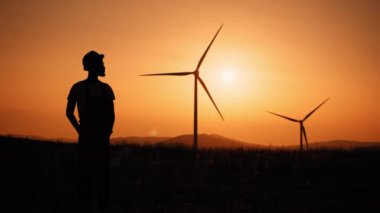 Yaz günbatımında elinde kocaman yel değirmenleriyle sahada duran siluet adam. Gelecek nesiller için temiz bir gelecek hayal etmek, çevre için temiz enerjinin canlandırıcı bir resmi..