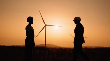 Siluetteki adam arka planda rüzgar türbinleri olan bir mühendisle tokalaşıyor. İki meslektaş başarılı bir iş birliği anlaşması yapıyor. Çevre için temiz enerjinin iç açıcı görüntüsü