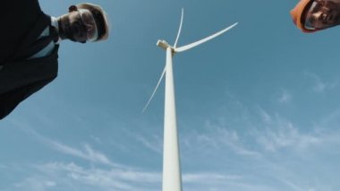 Beyaz miğfer ve siyah takım elbiseli Afro-Amerikan müfettişi büyük bir yel değirmeninin yanında dururken Hint mühendisiyle tokalaşıyor. Başarılı işbirliği, takım çalışması ve alternatif enerji kavramı