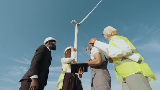 Multirassische Mitarbeiter, die sich auf einem Bauernhof mit Windmühlen treffen. Inspektor und Ingenieur inspizieren ein Projekt in einem Windkraftfeld, das Strom erzeugt. Sauberes Energiekonzept, erneuerbare Energien — Stockvideo