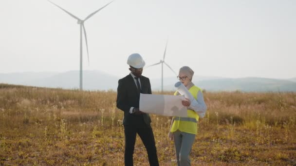 Bir grup profesyonel, temiz çevre dostu enerji üretmek için işbirliği yapıyor. Ekipte rüzgar türbinlerinin kurulum alanının planları var. İş adamı ve ekibi güç üretim alanını araştırıyor. — Stok video