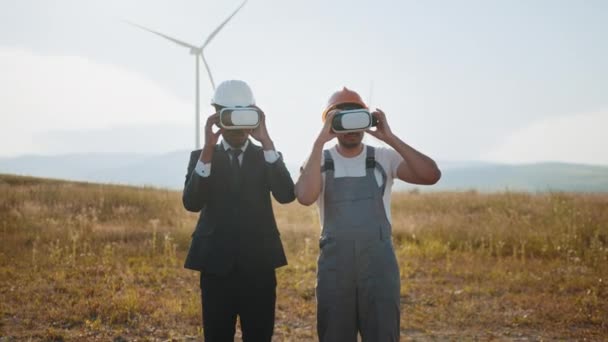 Amerikanischer Geschäftsmann und indischer Ingenieur mit VR-Headset bei einem Treffen auf einem Windkraftpark. Innovative Technologien und alternative Energiekonzepte. VR-Headset bei Treffen auf Öko-Bauernhof — Stockvideo