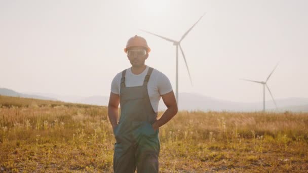 Muž v bílé helmě a černém obleku potřásá rukou s indiánským inženýrem s větrnými turbínami na pozadí. Diskuse o instalaci vyvíjí čisté pole elektrárny generátor větrné energie větrné turbíny — Stock video
