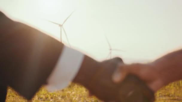 Close-up de diversos parceiros apertando as mãos entre moinhos de vento. Empresários e técnicos apertam a mão com negócios, trabalho bem sucedido, trabalho em equipe, energia limpa eólica da turbina. Instalação de turbinas eólicas — Vídeo de Stock