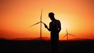 Siluet Afrikalı Amerikalı endüstriyel işçiler, rüzgar türbinleriyle çiftlikte dikilirken mobil konuşmalar yapıyorlar. Miğfer ve üniformalı uzman mühendis eko istasyonunda çalışıyor..