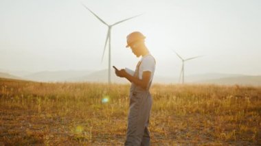 Afrika kökenli Amerikalı endüstriyel işçiler, rüzgar türbinleriyle çiftlikte dikilirken mobil konuşmalar yapıyorlar. Kasklı ve üniformalı bir mühendis eko istasyonunda çalışıyor. Rüzgar türbinleri olan bir adam.