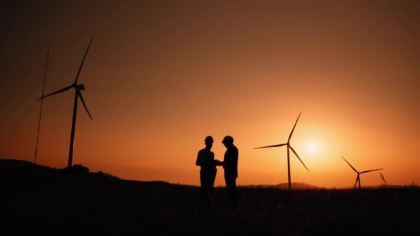 Silhouette Ingenieur und Inspektor arbeiten zusammen auf dem Windmühlenpark. Ingenieur und indischer Inspektor mit digitalem Tablet bei Treffen im Freien. Zwei Partner stehen mit Windrädern auf dem Feld — Stockvideo