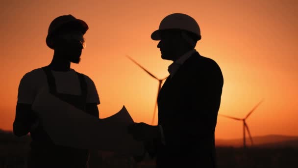 Silhouette Close up face two professionals technicians in hard hat using a large blueprint. Engineers working discussing on ecological station. Wind turbine power station. Wind turbines blueprints. — Stock Video