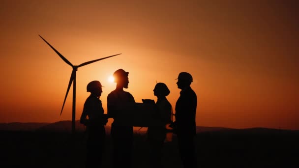 Tim Silhouette Internasional mitra bisnis berdiri bersama di antara turbin angin dan memeriksa cetak biru. Kelompok profesional bekerja sama untuk menghasilkan energi ramah lingkungan. Turbin angin — Stok Video