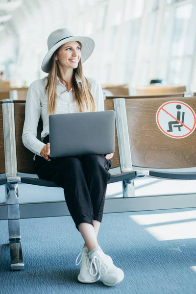 Nainen odottaa lentoa lentokentän terminaalissa, istuu tuolilla ja kirjoittaa kannettavan näköinen puolella. Yläkuva . — kuvapankkivalokuva