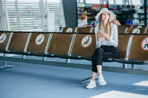 Kaunis liikenainen naamiossa lentokentällä puhelimella lähettää tekstiviestejä yrityksen toimistorakennuksessa, tarkistamalla sähköpostit Internetissä, menestyvä naisjohtaja töissä — kuvapankkivalokuva