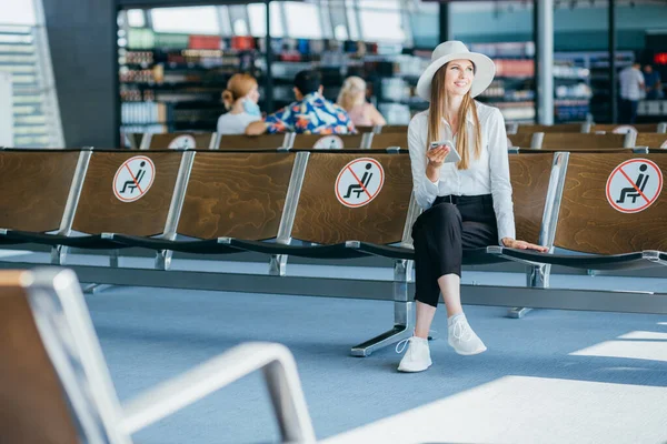 Nainen älypuhelimessa, odotusaika terminaalissa, käytä matkasovellusta, hymyillen. — kuvapankkivalokuva