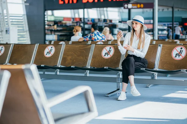 Matkailu turisti nainen seisoo matkatavaroiden tarkistaa lennon numero älypuhelin lentokentällä. Nuori liikemies matkalaukkuineen odottaa lähtöportilla ennen lähtöä. Matkailuelämäntapa — kuvapankkivalokuva