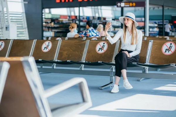 Das junge Hipster-Mädchen fotografiert sich mit dem Handy, während es sich in einem modernen Café in der Nähe des Seehafens entspannt. Attraktive Frau mit Kaffee zum Mitnehmen fotografiert mit Smartphone-Kamera — Stockfoto