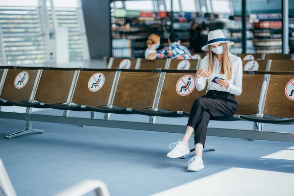 Ung student collegejente som sitter på flyplassen bærer medisinsk maske og er fornøyd med en sikkerhetsreise-bobleplan etter en kald pandemi og venter på at flyet skal være i stand til å fly i Asia. – stockfoto