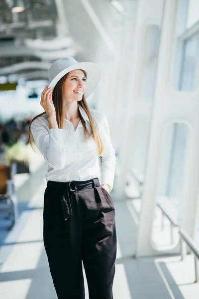 หญิงสาวที่เจ๋งในเรือและชุดสีขาวยิ้มและมองเข้าไปในกล้องด้านนอก นักท่องเที่ยวถือพาสปอร์ตและโพสบนทางเดินใกล้สนามบิน — ภาพถ่ายสต็อก