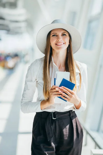 Iloinen liikenainen odottaa lentoa lentokentällä. Nuori nainen lentokentällä. Nuori nainen, jolla on passi ja tarkastuskortti lentokentällä. Muoti nainen muotokuva. Liikenainen lentoliikenteessä — kuvapankkivalokuva