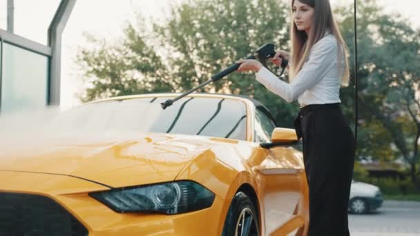 Servicio de lavado de coches al aire libre. Caucásico seguro de sí mismo elegante mujer de negocios europea lavando coche de lujo amarillo con pistola de agua en un auto-lavado al aire libre. concepto de lavado de coches. Servicio de coches. — Vídeo de stock