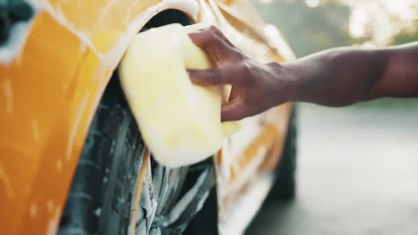 Hands of African man holding yellow sponge, washing car wheel with foam. Cleaning of modern rims of luxury yellow car at self car wash service outdoors. Clean car concept. Foaming after rubbing. — Stock Video