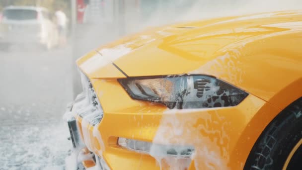 Vízpermet autómosáshoz és -tisztításhoz. A luxus sárga járművét nagynyomású vízszivattyúval mossa a szabadtéri autótisztítóban. Tiszta autó koncepció. Autómosó szabadtéren. — Stock videók