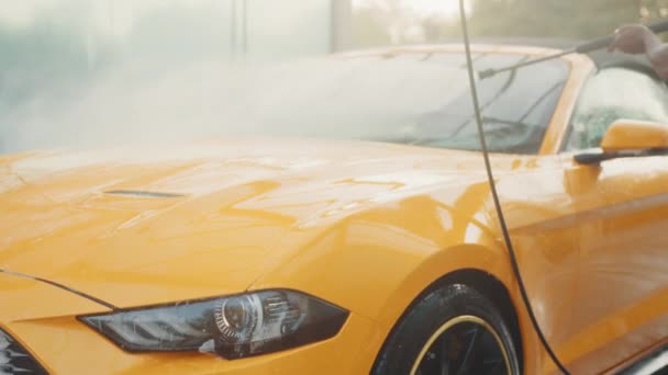 Tvätta hans lyxiga gula fordon med högtrycks vattenpump på bil rengöring självbetjäning utomhus. Rent bilkoncept. Biltvätt utomhus. Vatten sprider sig när man sprutar in i bilen. — Stockvideo