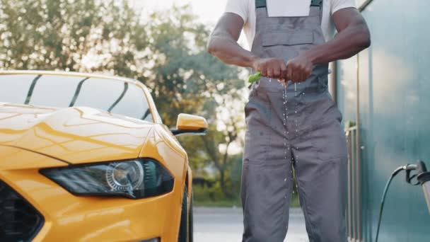 Ritaglio primo piano di bel barbuto giovane lavoratore africano svita uno straccio, su uno sfondo di auto giallo di lusso moderno. Un uomo che pulisce auto con un panno in microfibra. L'uomo tiene in mano la microfibra. — Video Stock