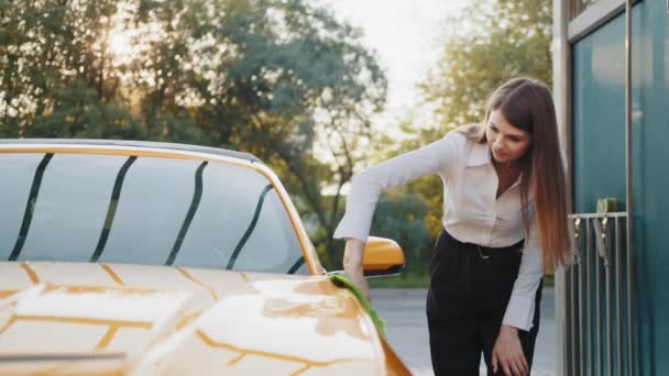 Lavage et nettoyage de voitures à la station libre-service extérieure. Prise de vue de la femme d'affaires réussie nettoyant sa capuche de voiture jaune avec un chiffon vert en microfibre à l'extérieur en été matin ensoleillé. Concept de voiture propre — Video