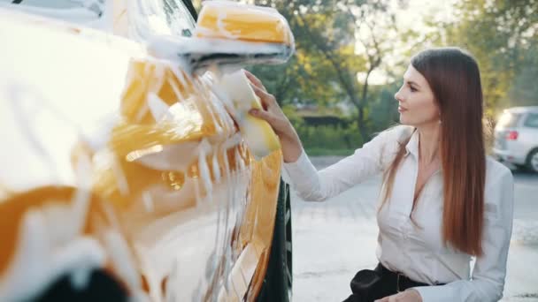Lyxig gul bil i tvålskum utomhus vid biltvättservice. Sidovy av kaukasiska affärskvinna på vit skjorta och svarta byxor med gul svamp för rengöring bildörr med tvålskum. Ren bil . — Stockvideo