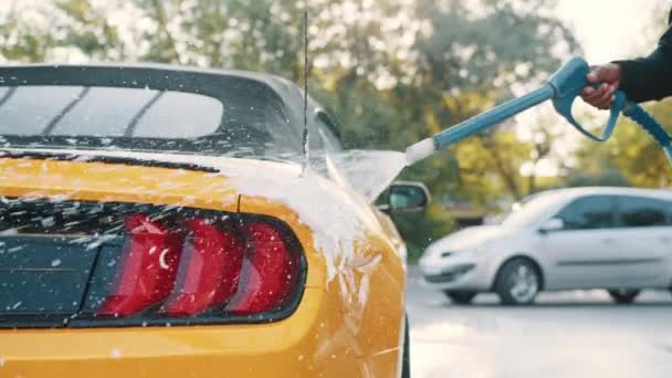Araba yıkama konsepti. Köpüklü sarı araba. Araba sabunla yıkanıyor. Yüksek basınçlı jeti olan Afrikalı bir adam benzin istasyonundaki sarı arabaya sabun püskürtüyor. Dışarıda araba yıkama. — Stok video